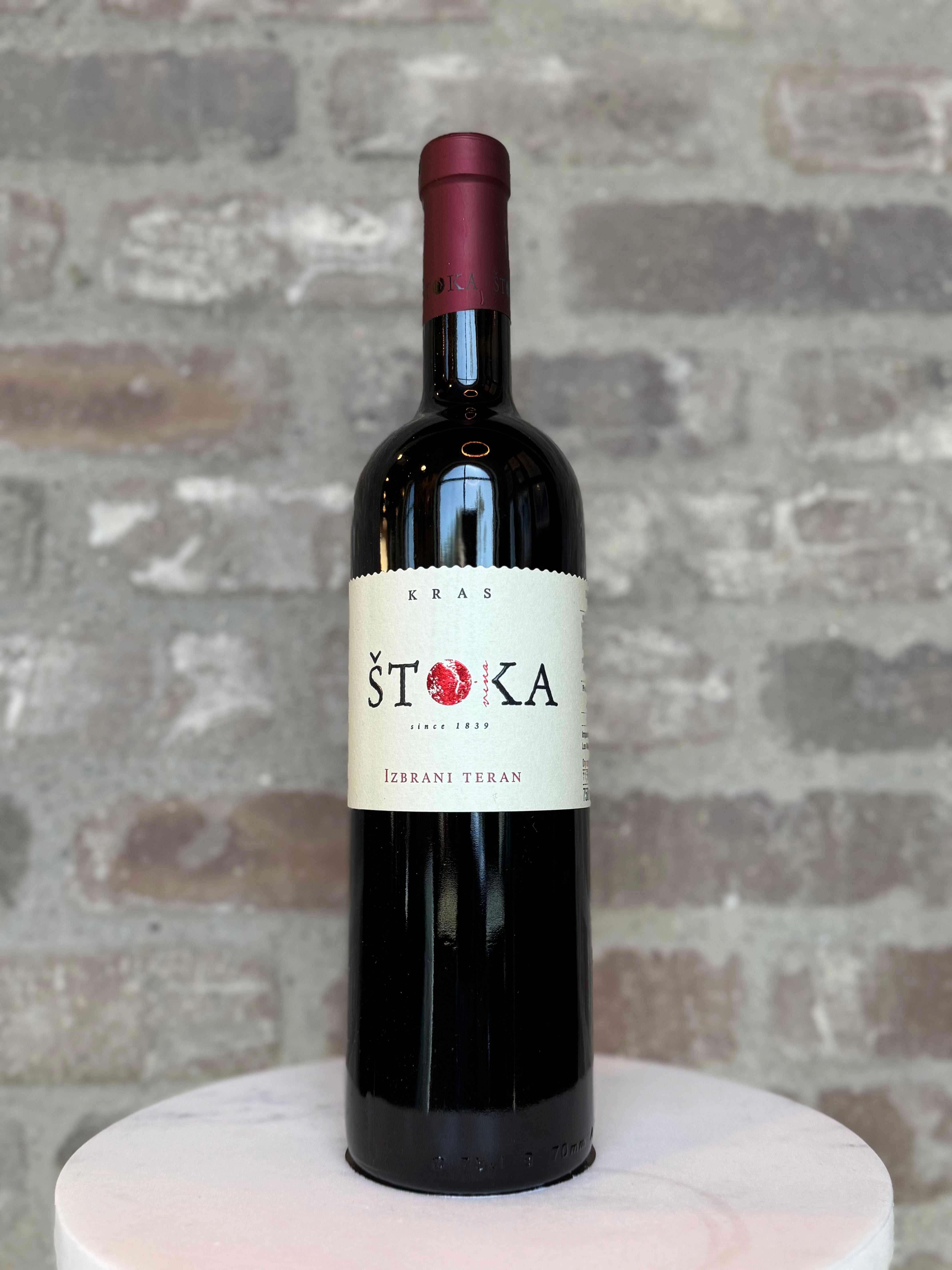 Bottle of Stoka wine on a white pedestal with a brick wall background