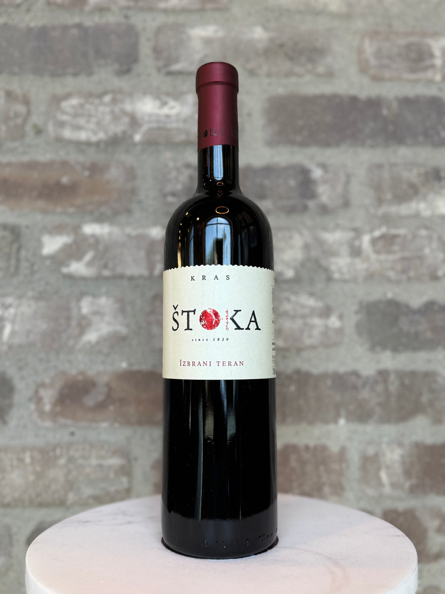 Bottle of Stoka wine on a white pedestal with a brick wall background