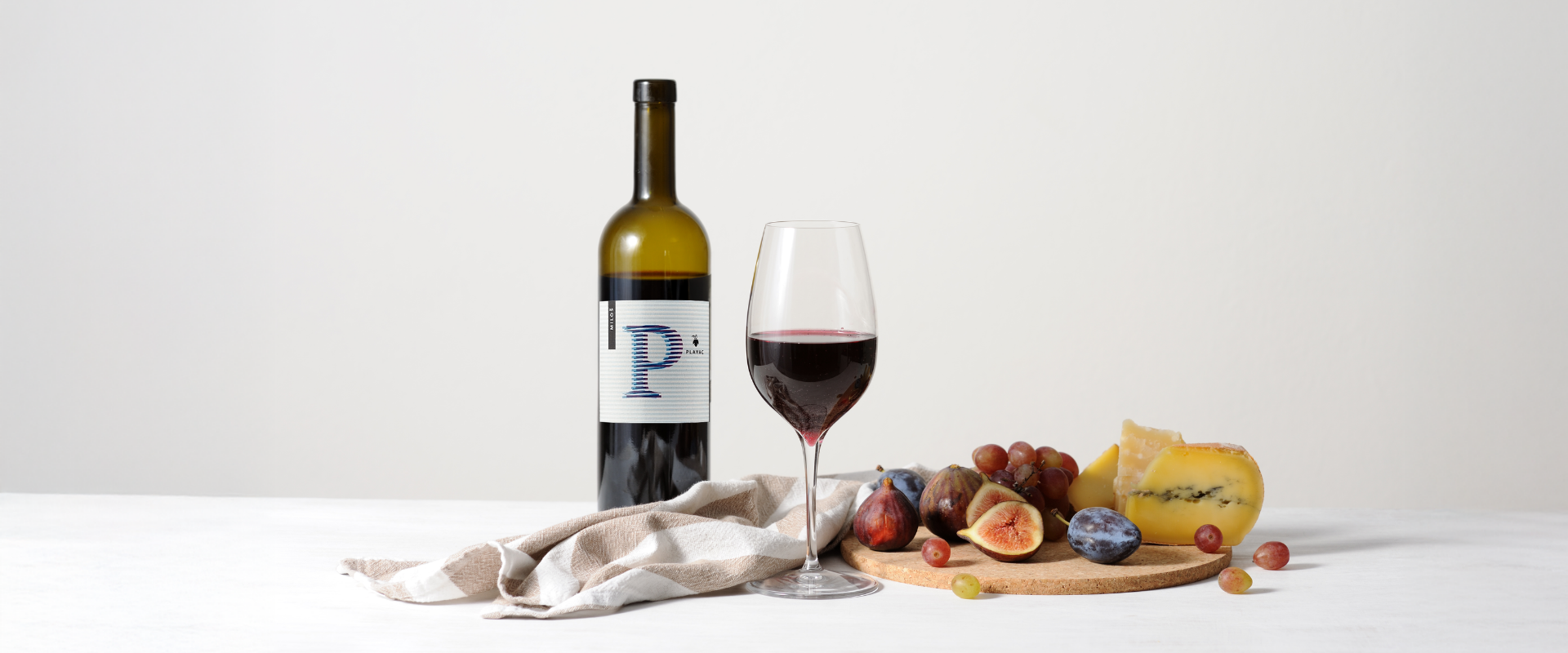 Wine bottle with a glass of red wine, cheese, and fruits on a white background