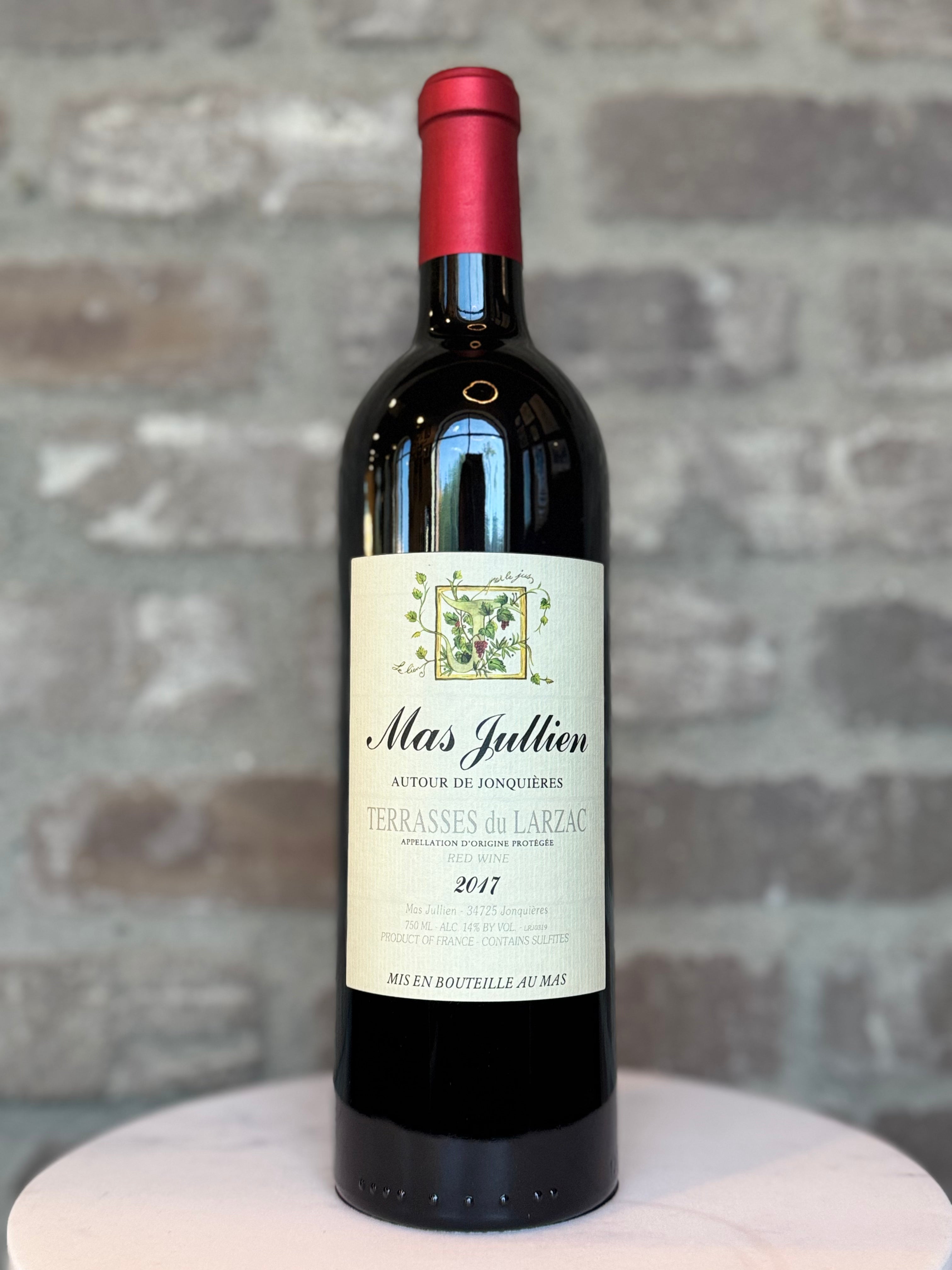 Wine bottle labeled 'Mas Julien' on a textured surface with a stone wall background