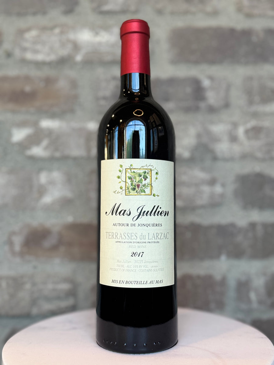 Wine bottle labeled 'Mas Julien' on a textured surface with a stone wall background