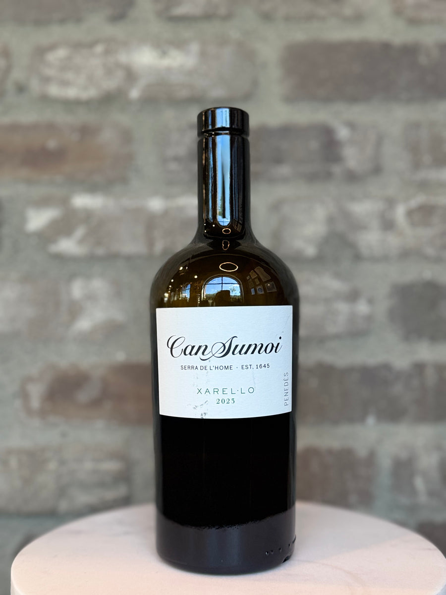 Wine bottle labeled 'Can Sumoi' on a stone surface with a stone wall background