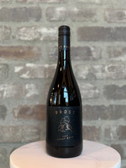 Wine bottle labeled 'Prost' on a white pedestal with a gray brick background