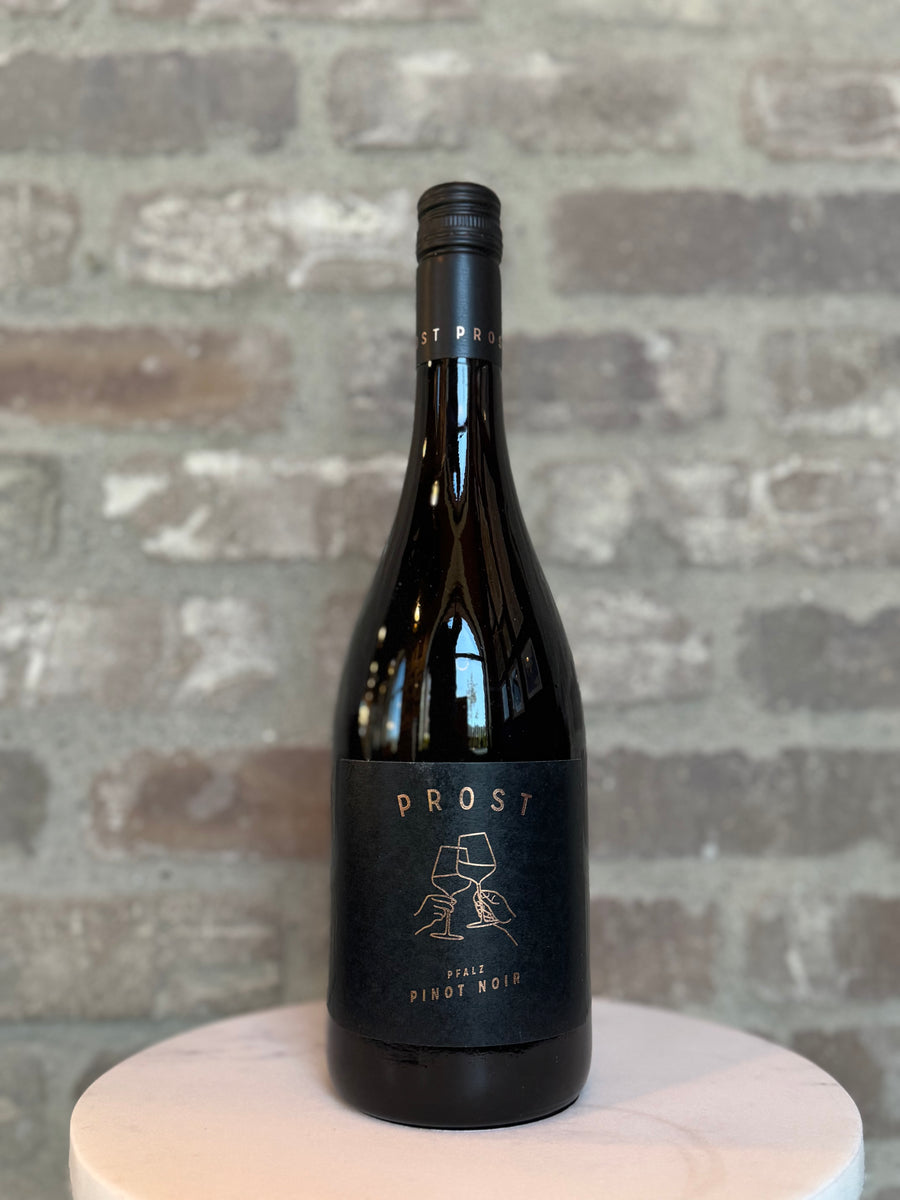 Wine bottle labeled 'Prost' on a white pedestal with a gray brick background