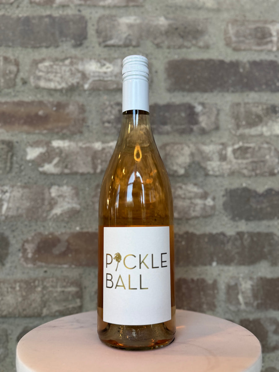 Bottle of Pickle Ball wine on a wooden stand with a brick wall background