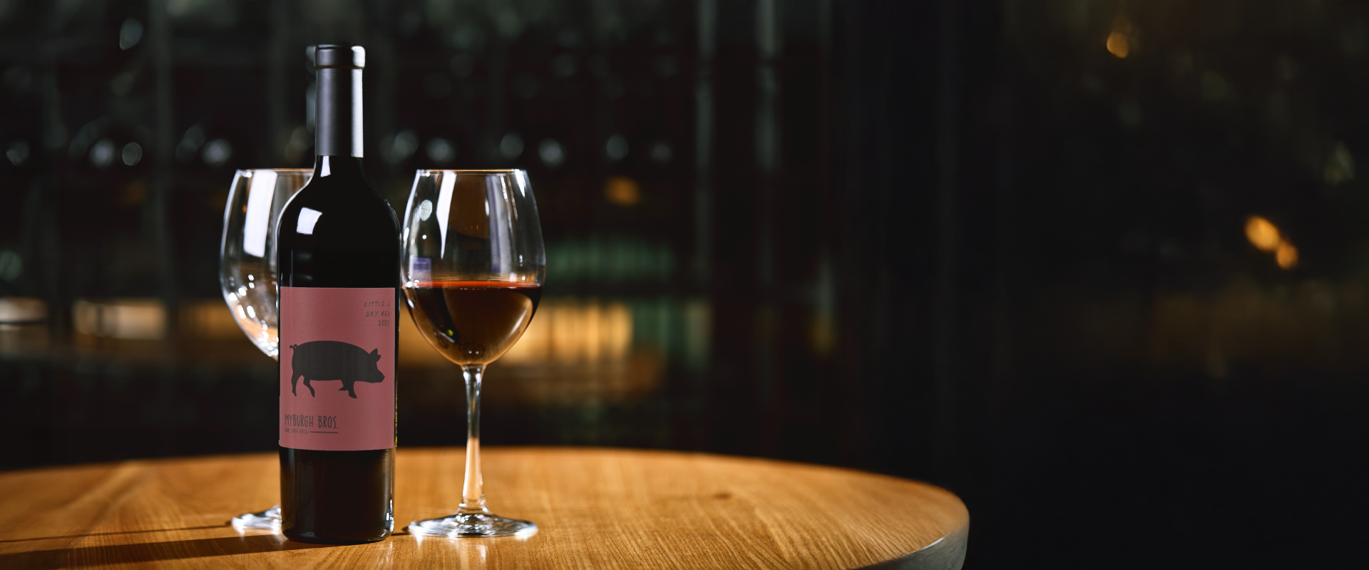 Wine bottle with a pink label and wine glass on a wooden table with a dark background