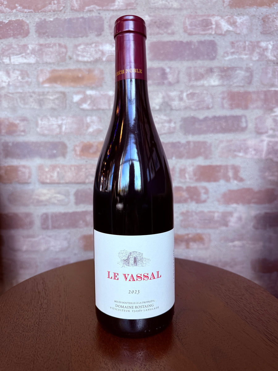 Wine bottle labeled 'Le Vassal' on a wooden surface with a brick wall background