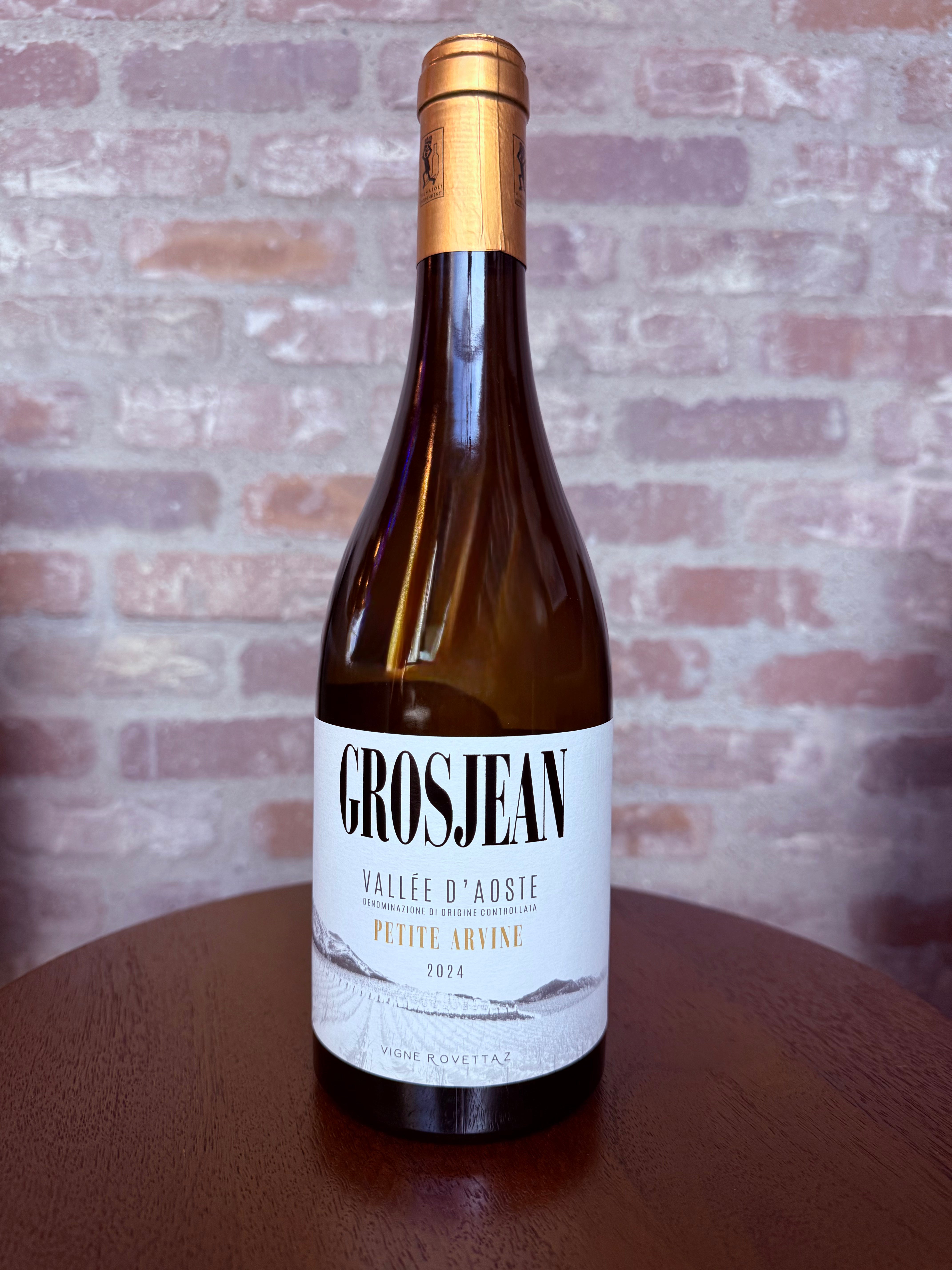 Wine bottle with 'Grosjean' label on a wooden surface with a brick wall background
