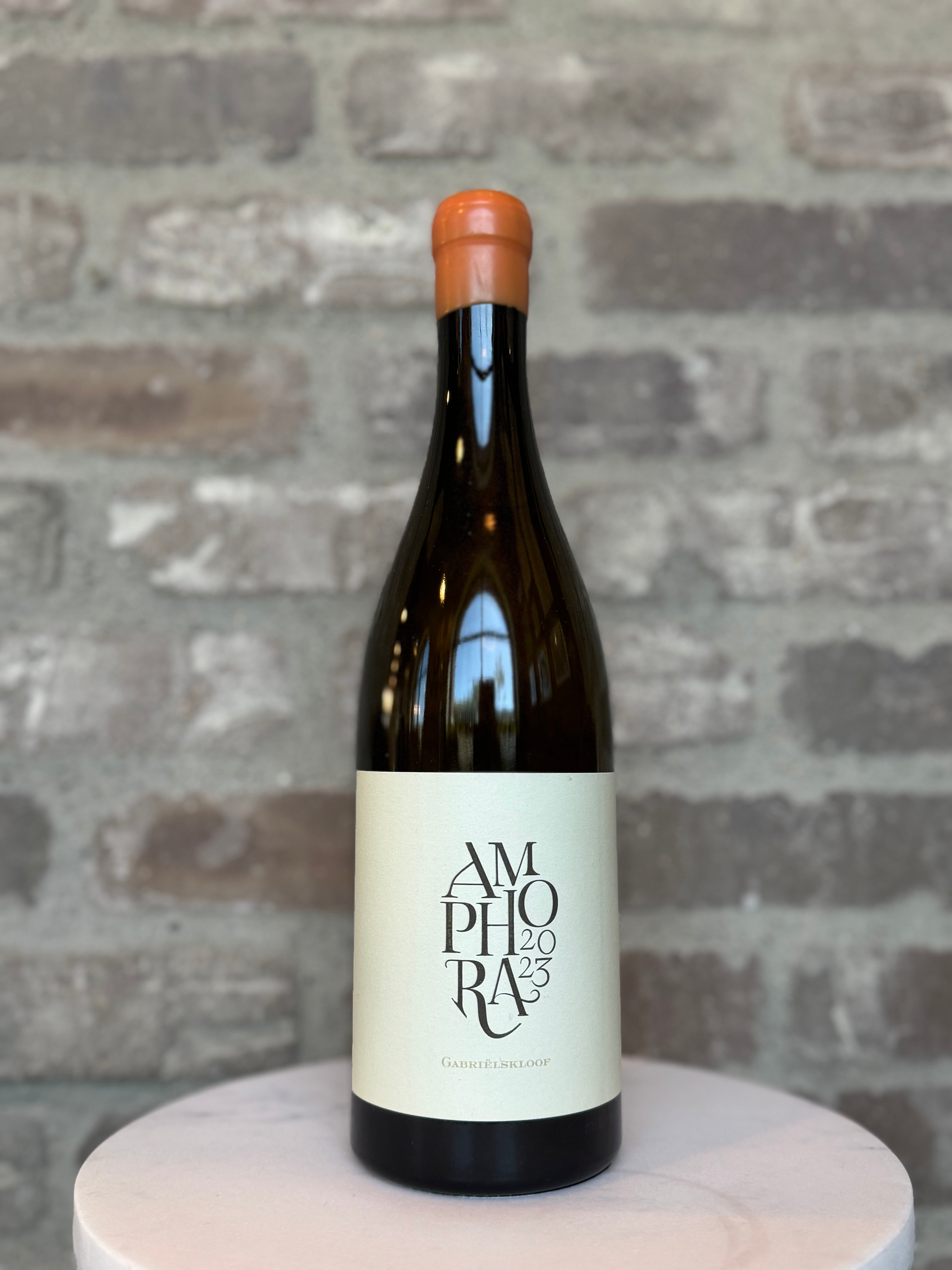 Wine bottle labeled 'Amphora 2023' on a round wooden platform with a brick wall background