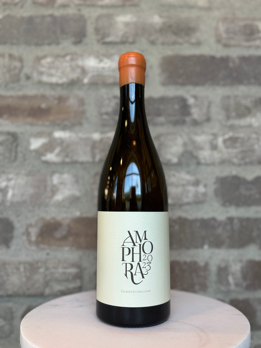Wine bottle labeled 'Amphora 2023' on a round wooden platform with a brick wall background