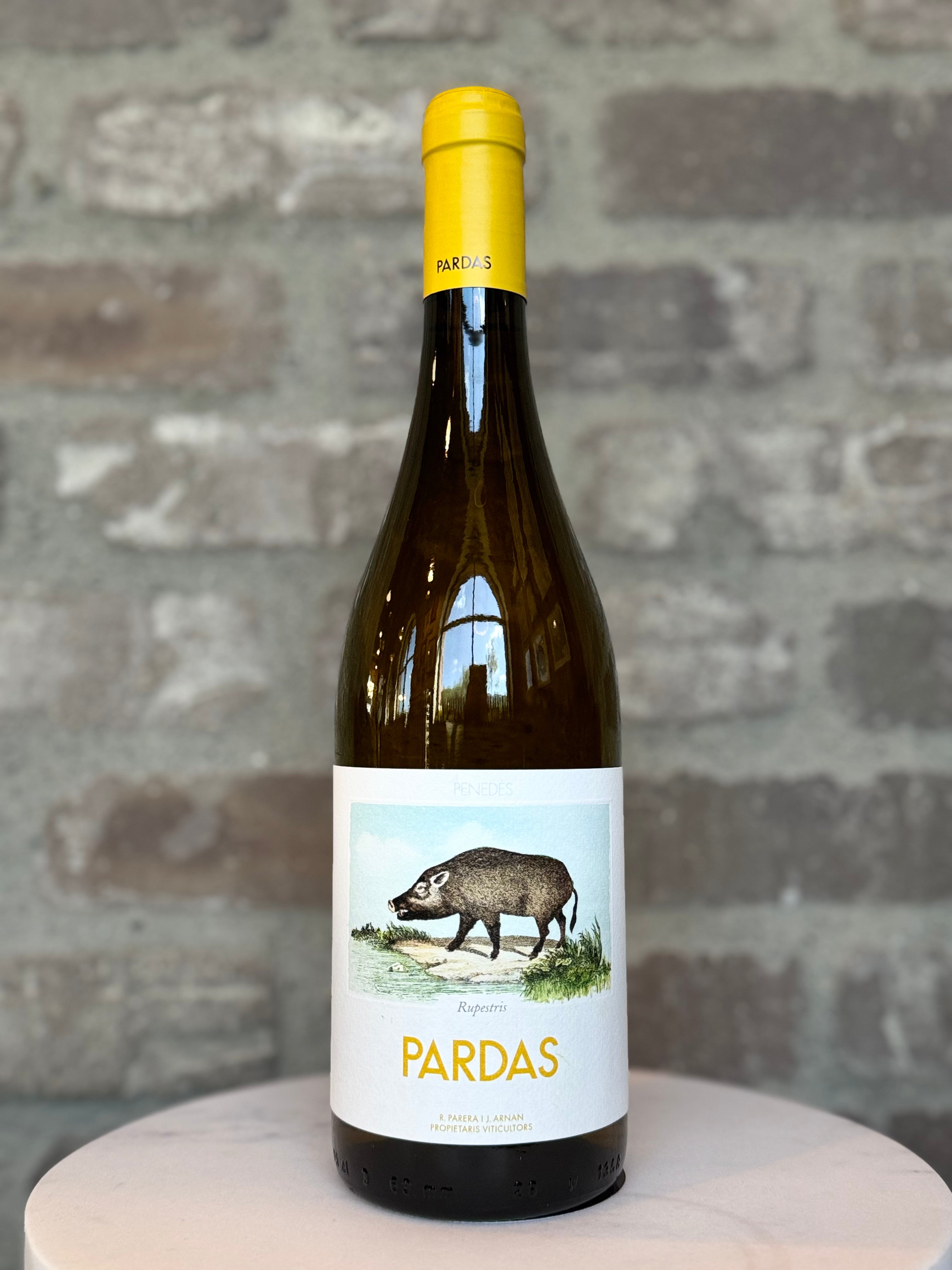 Wine bottle with a yellow cap and white label featuring an illustration of a boar, against a stone wall background.