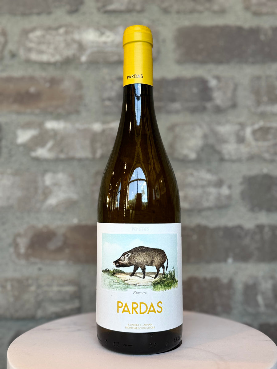 Wine bottle with a yellow cap and white label featuring an illustration of a boar, against a stone wall background.