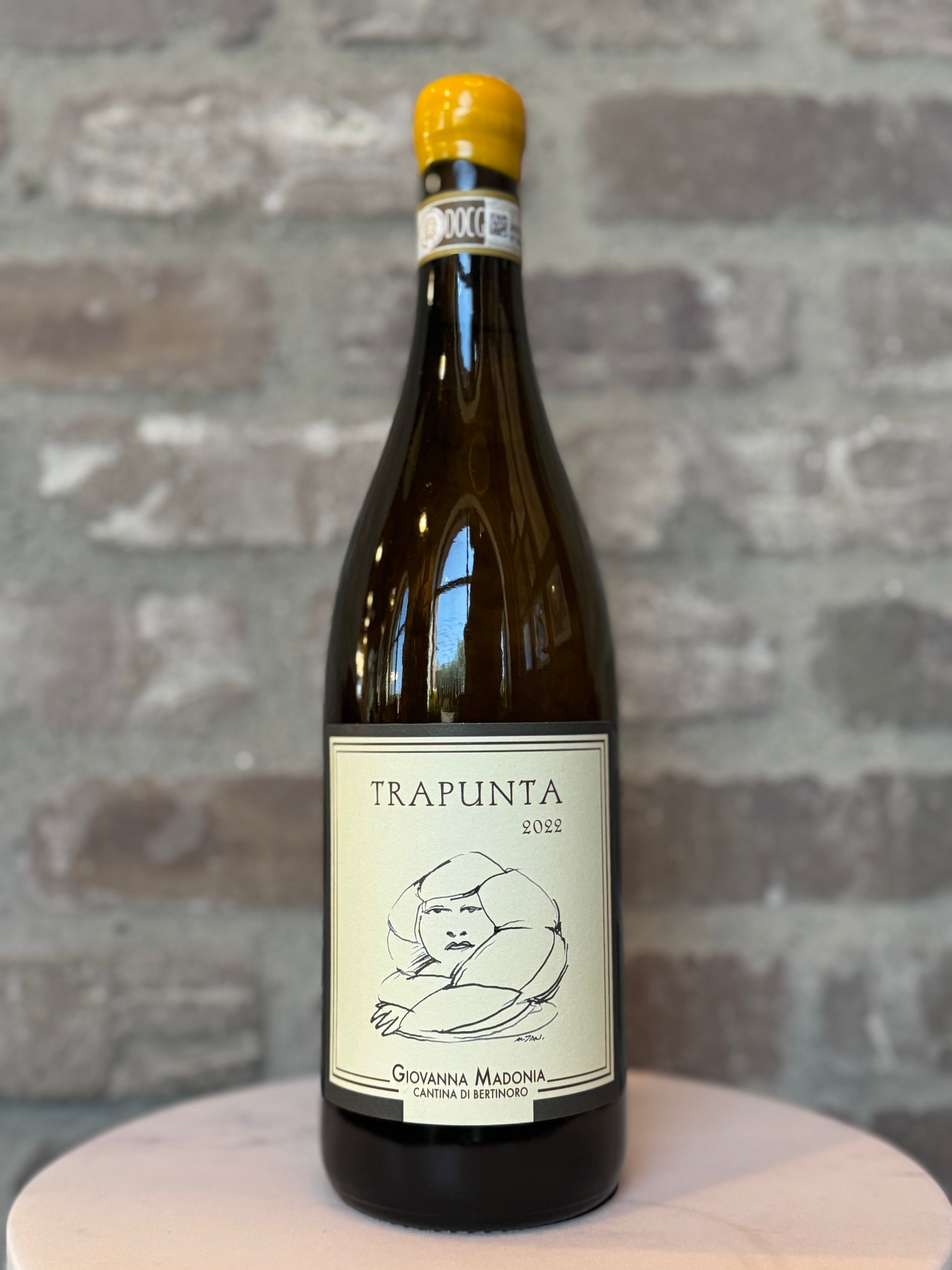 Bottle of Trapunta wine on a wooden surface with a stone wall background