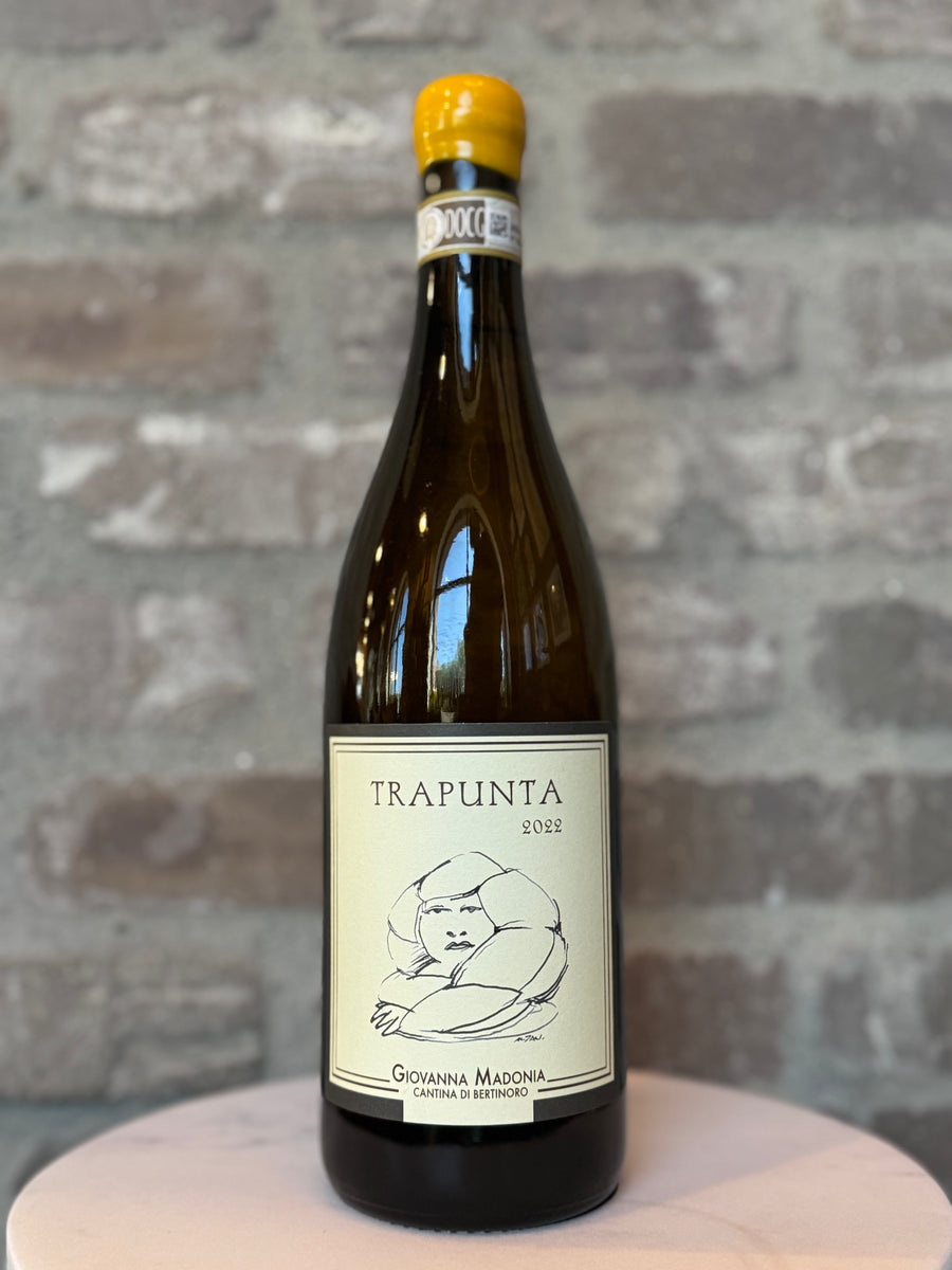 Bottle of Trapunta wine on a wooden surface with a stone wall background