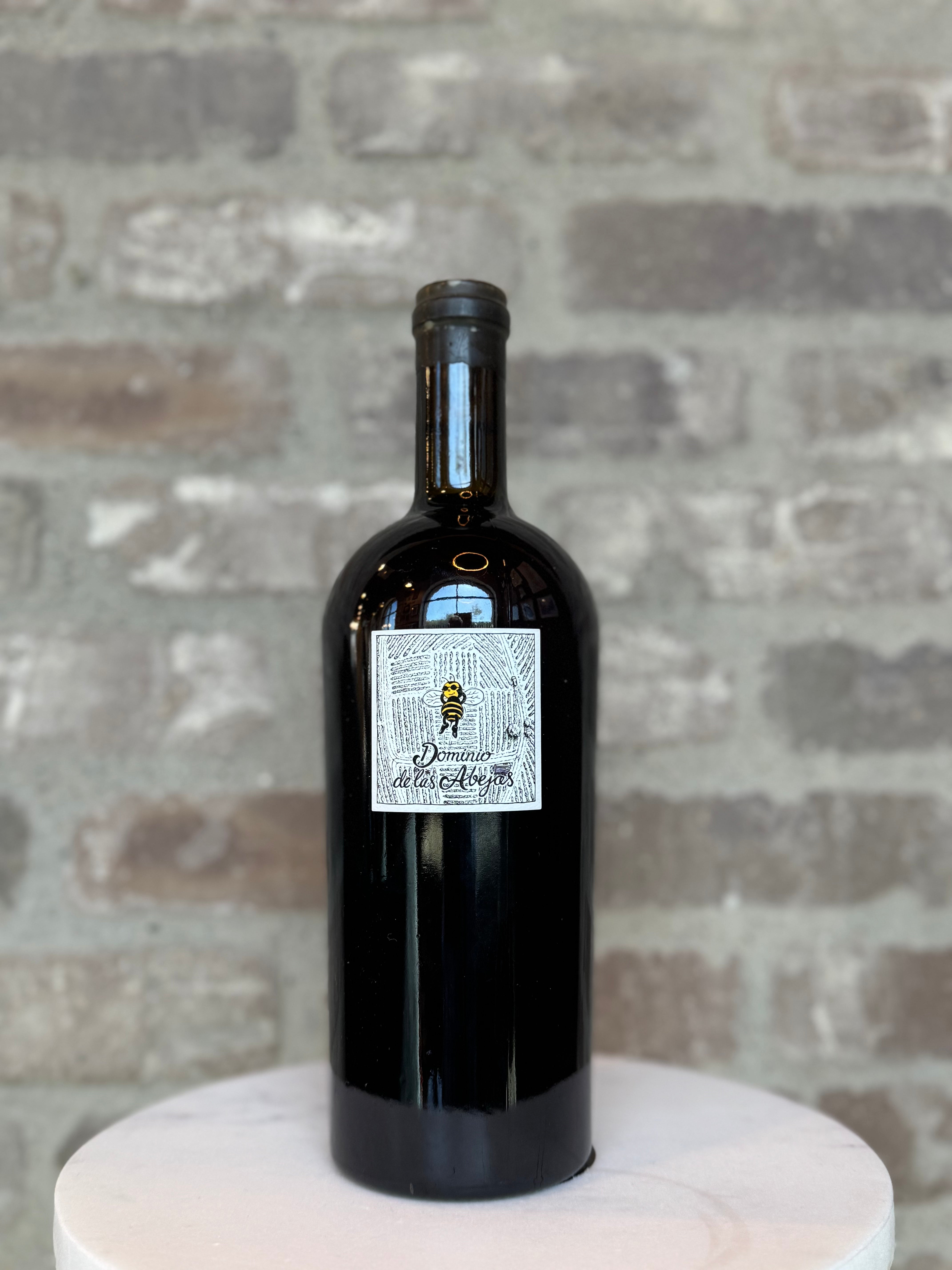 Black wine bottle with a label on a white pedestal against a stone wall background