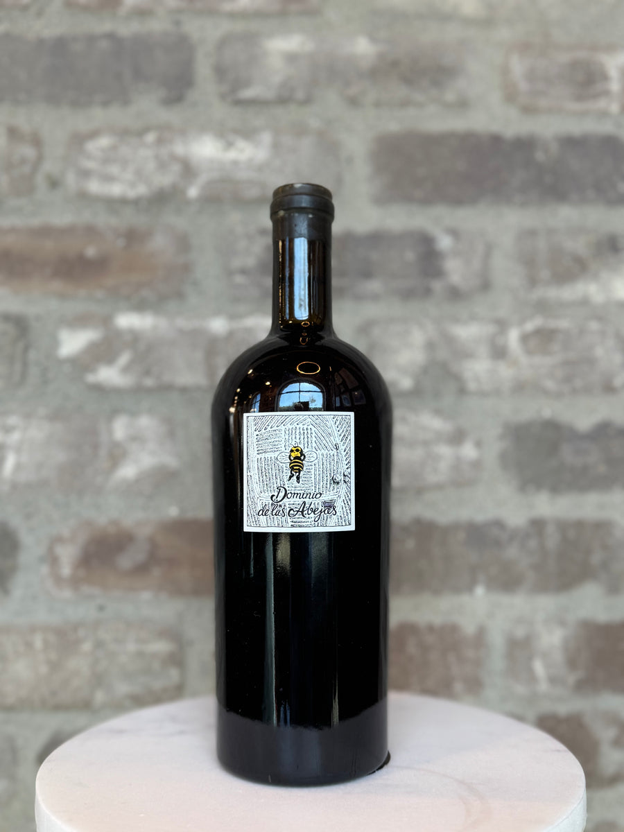 Black wine bottle with a label on a white pedestal against a stone wall background