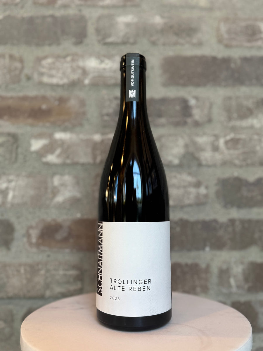 Wine bottle labeled 'Trollinger Alte Reben' on a wooden stand with a brick wall background