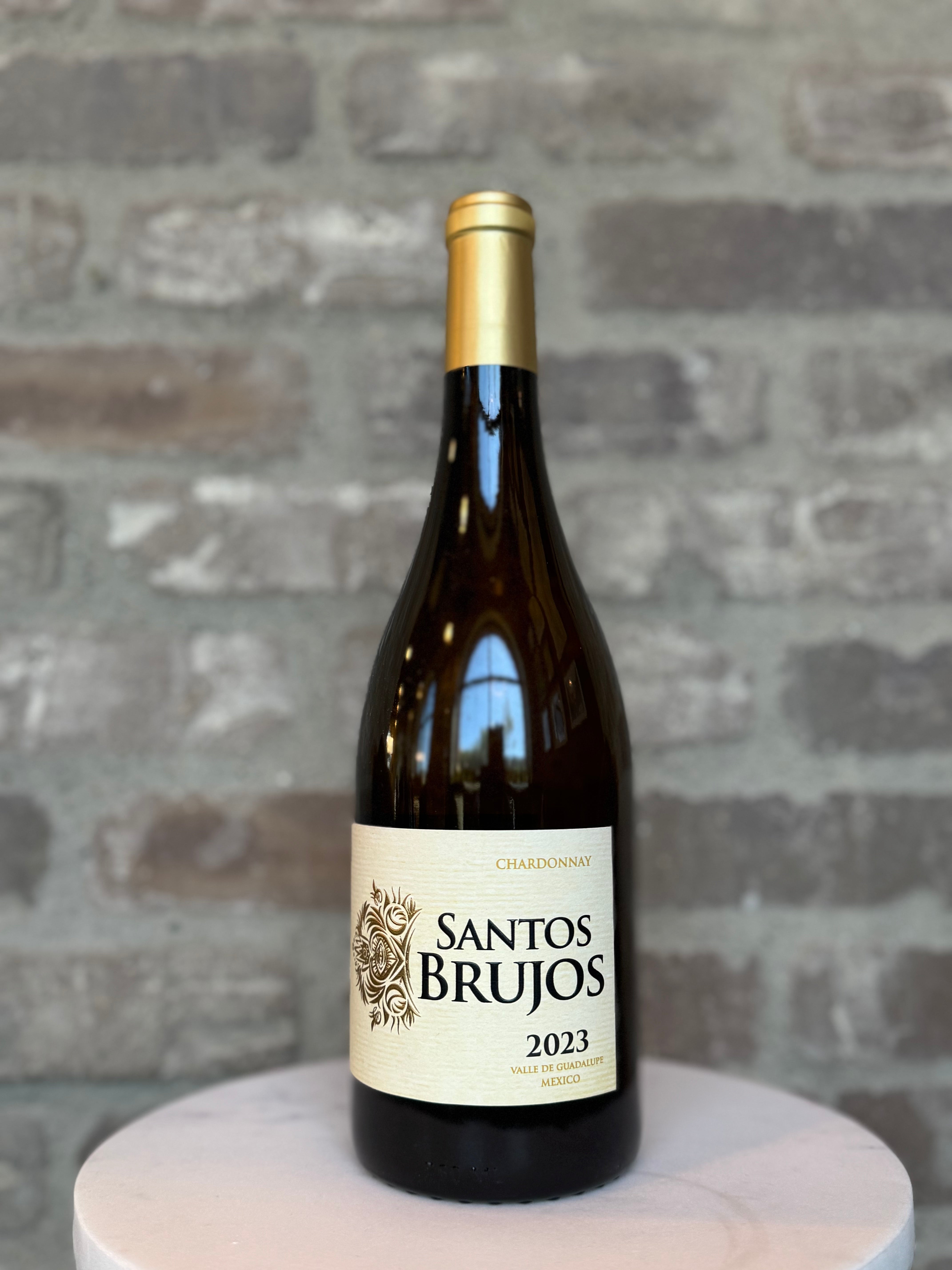 Bottle of Santos Brujos 2023 wine on a wooden stand with a stone wall background