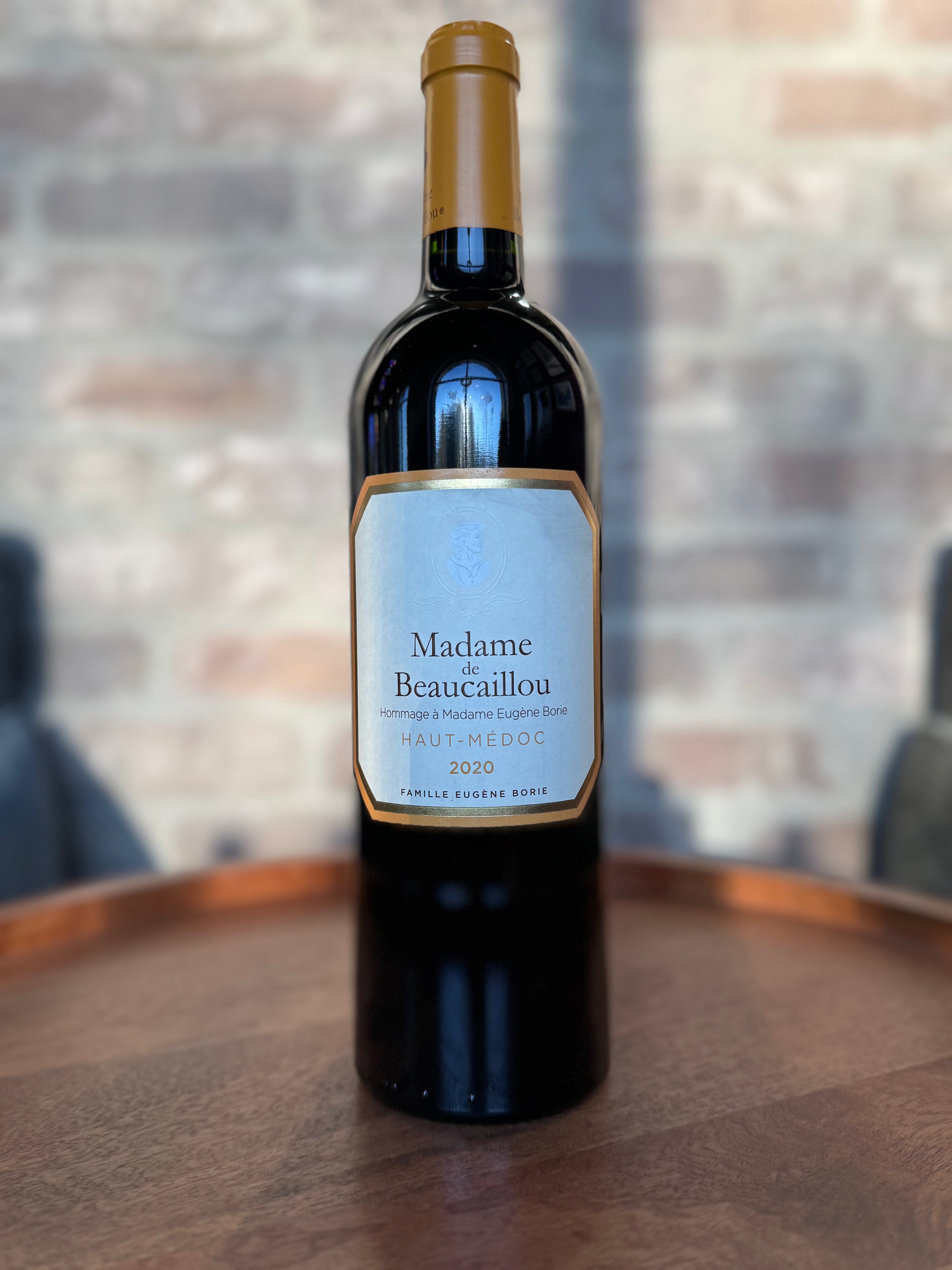 Wine bottle labeled 'Madame Beaucailou' on a wooden surface with a blurred background