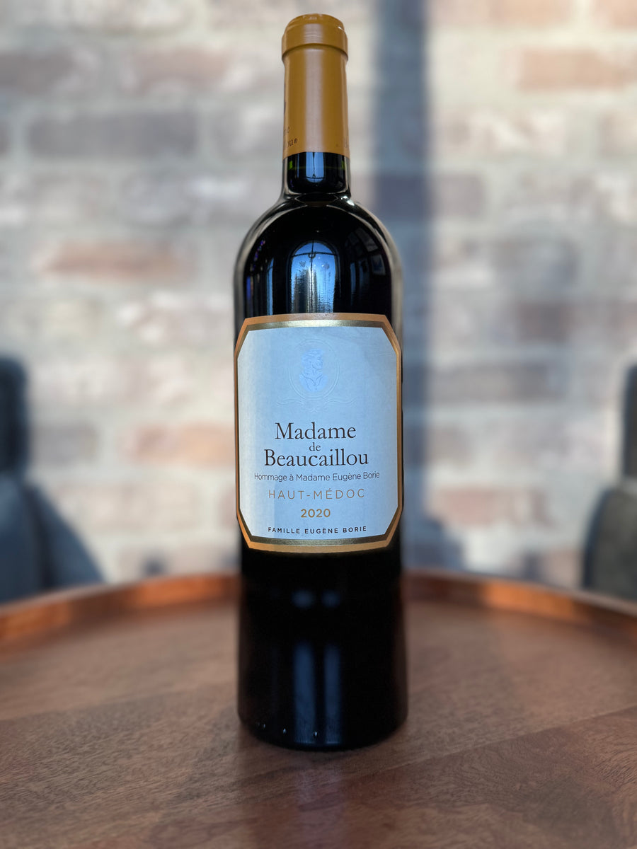 Wine bottle labeled 'Madame Beaucailou' on a wooden surface with a blurred background