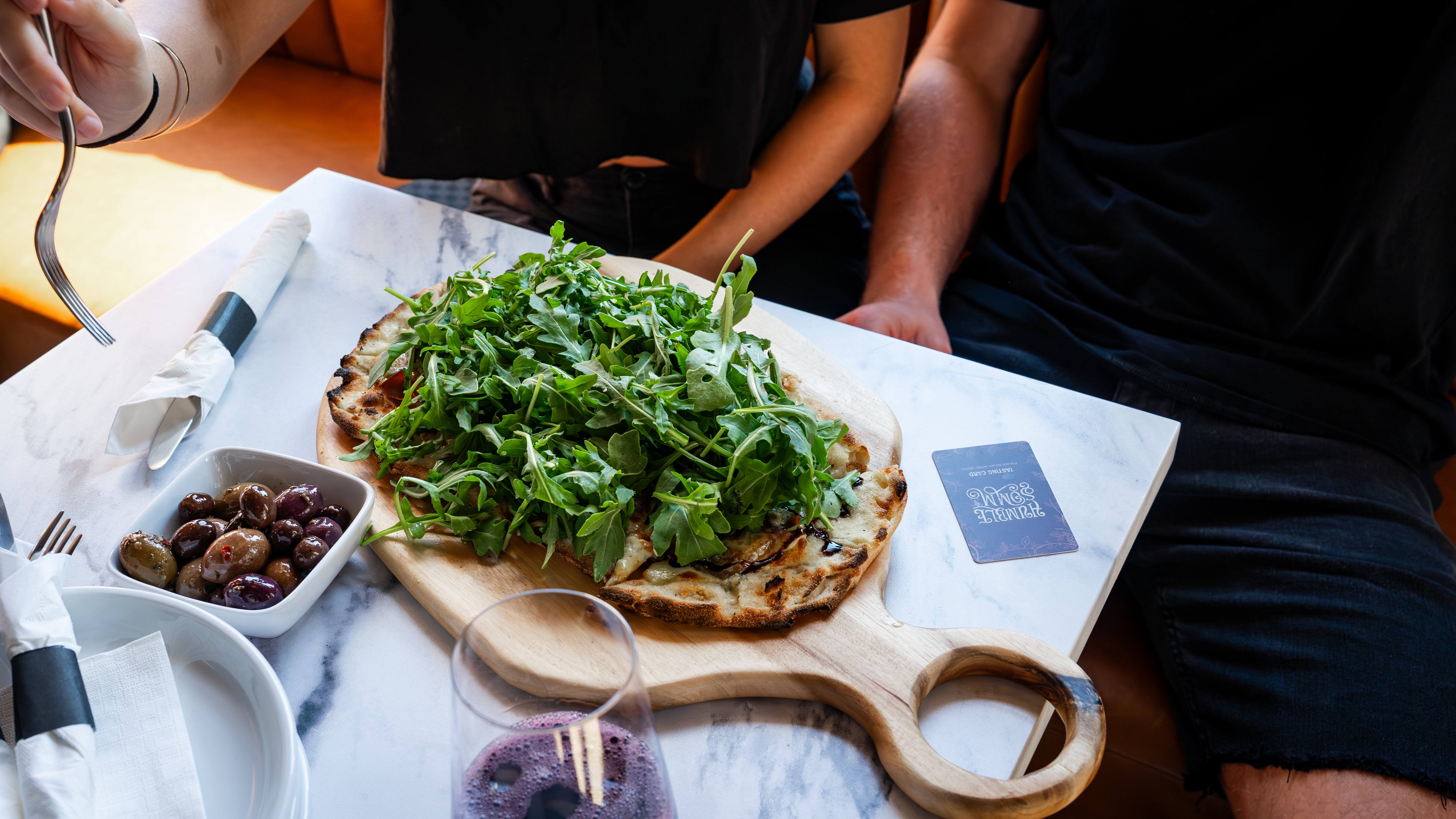 Person sitting at a table with a pizza topped with arugula and figs.