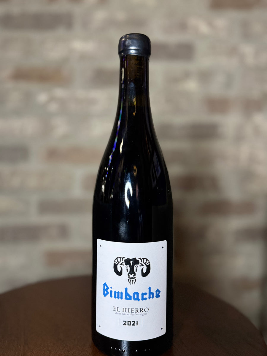 Wine bottle with 'Bimbache' label on a wooden surface against a brick wall background