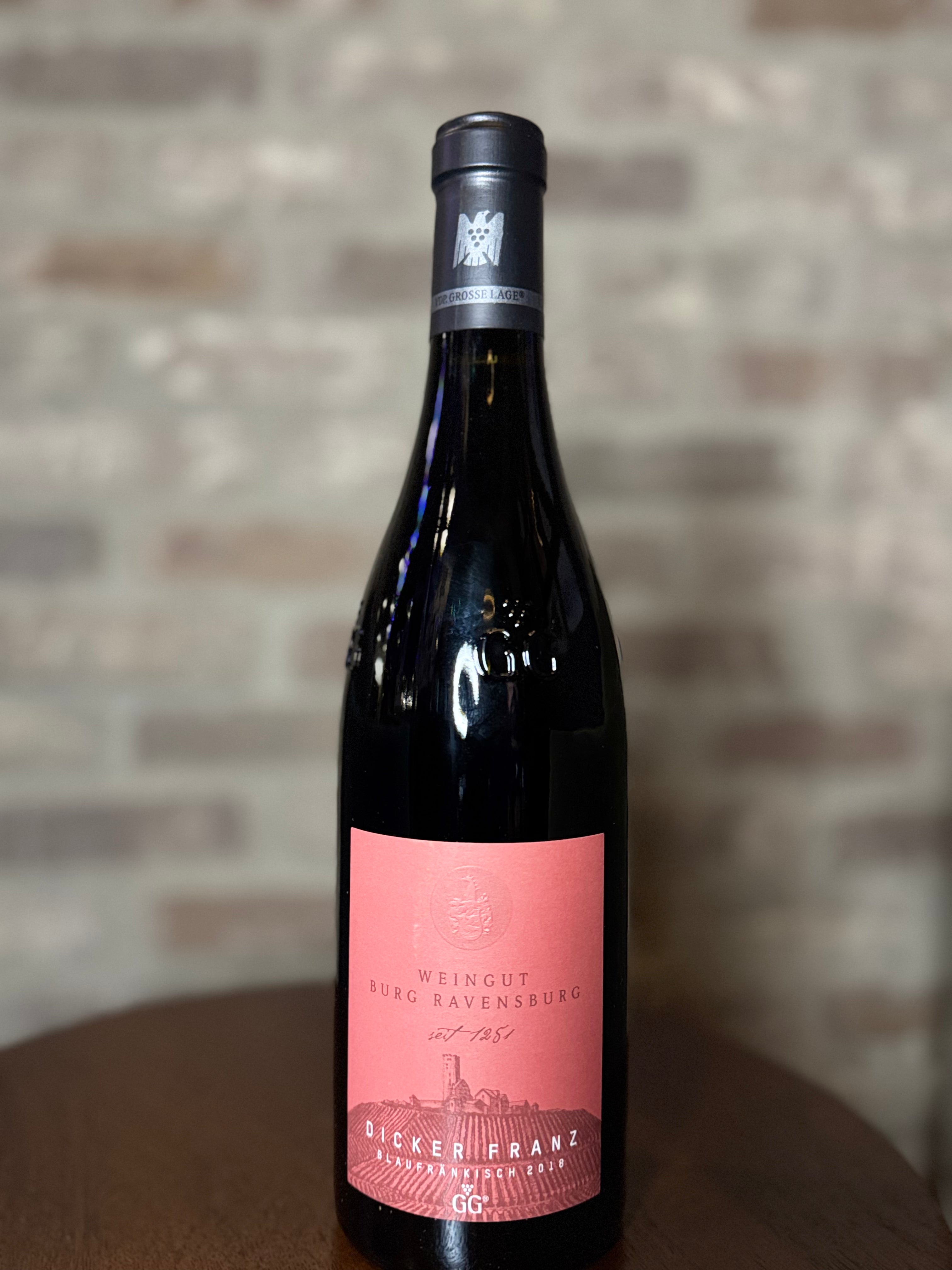 Wine bottle with a pink label on a wooden surface against a brick wall background