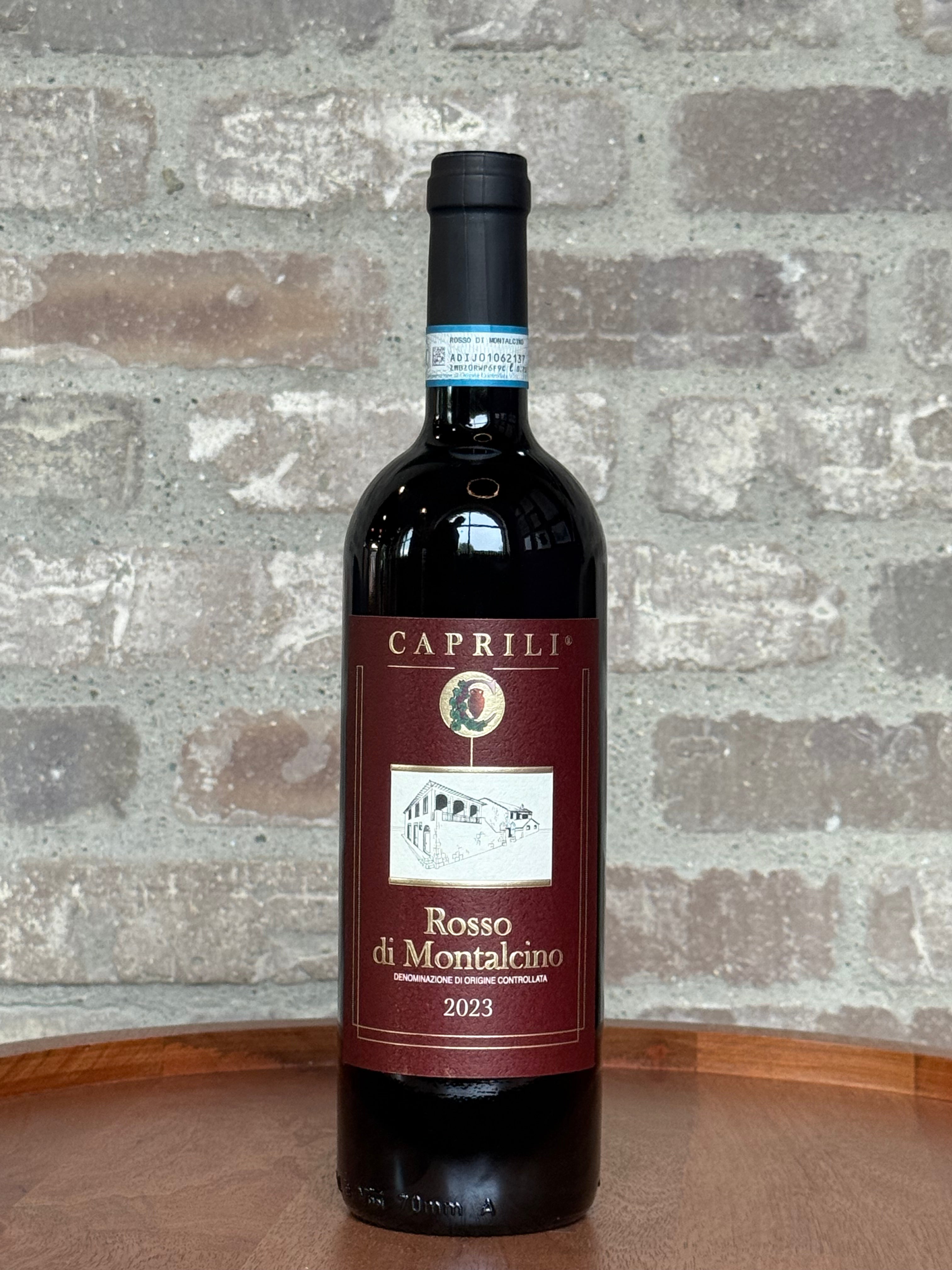 Wine bottle labeled 'Caprili Rosso di Montalcino 2023' on a stone surface with a stone wall background