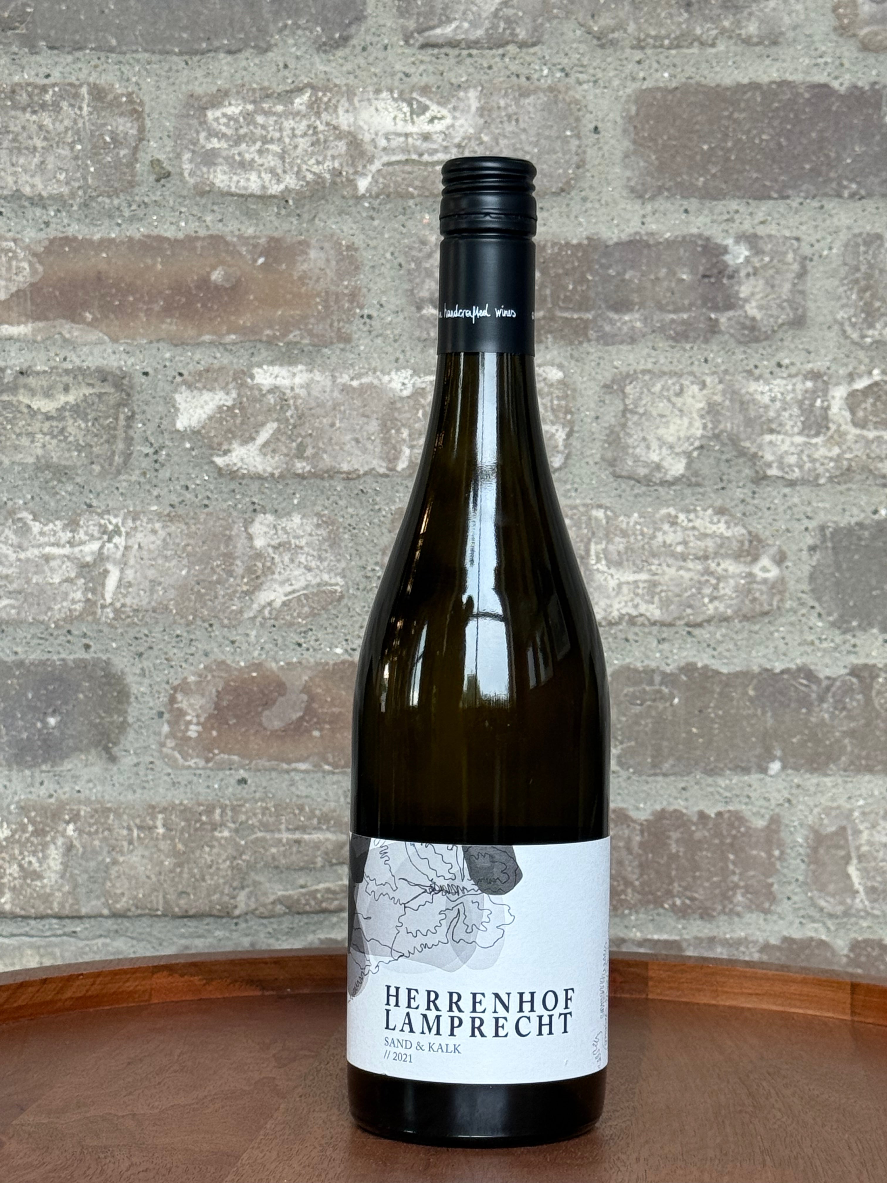 Wine bottle labeled 'Herrenhof Lamprecht' on a wooden surface with a stone wall background