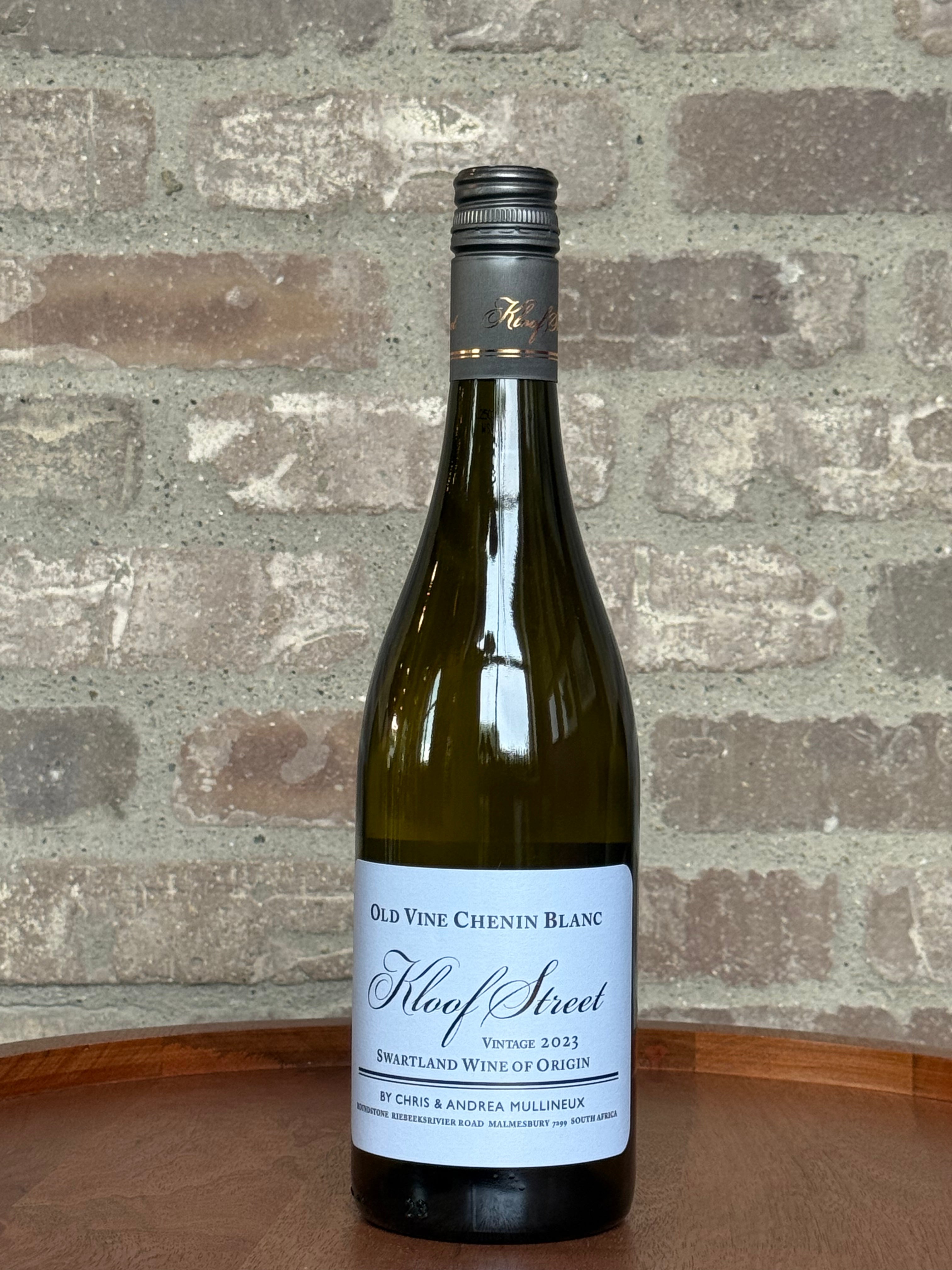 Bottle of Old Vine Chenin Blanc wine on a wooden surface with a stone wall background