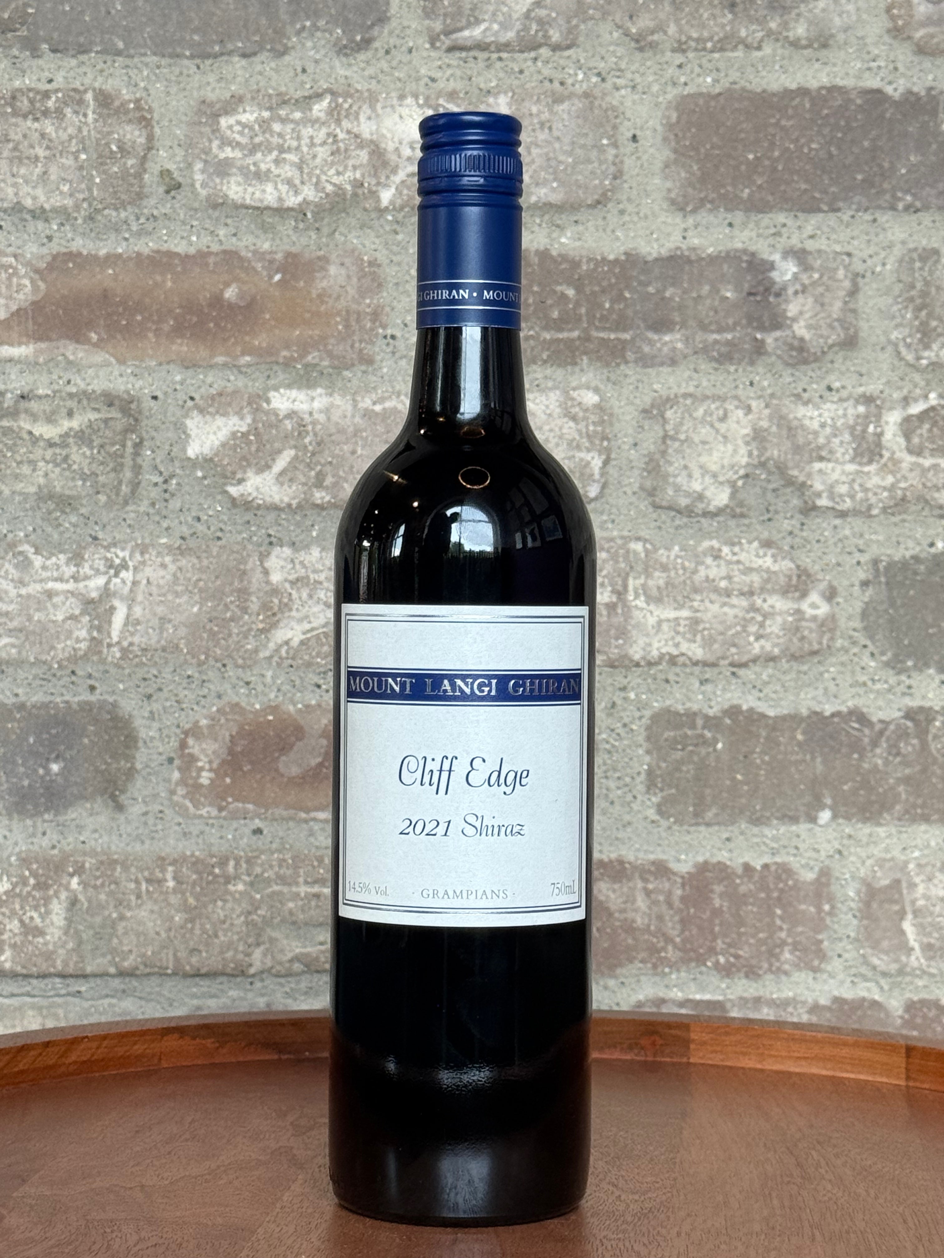 Wine bottle labeled 'Cliff Edge' with a blue cap on a stone surface.