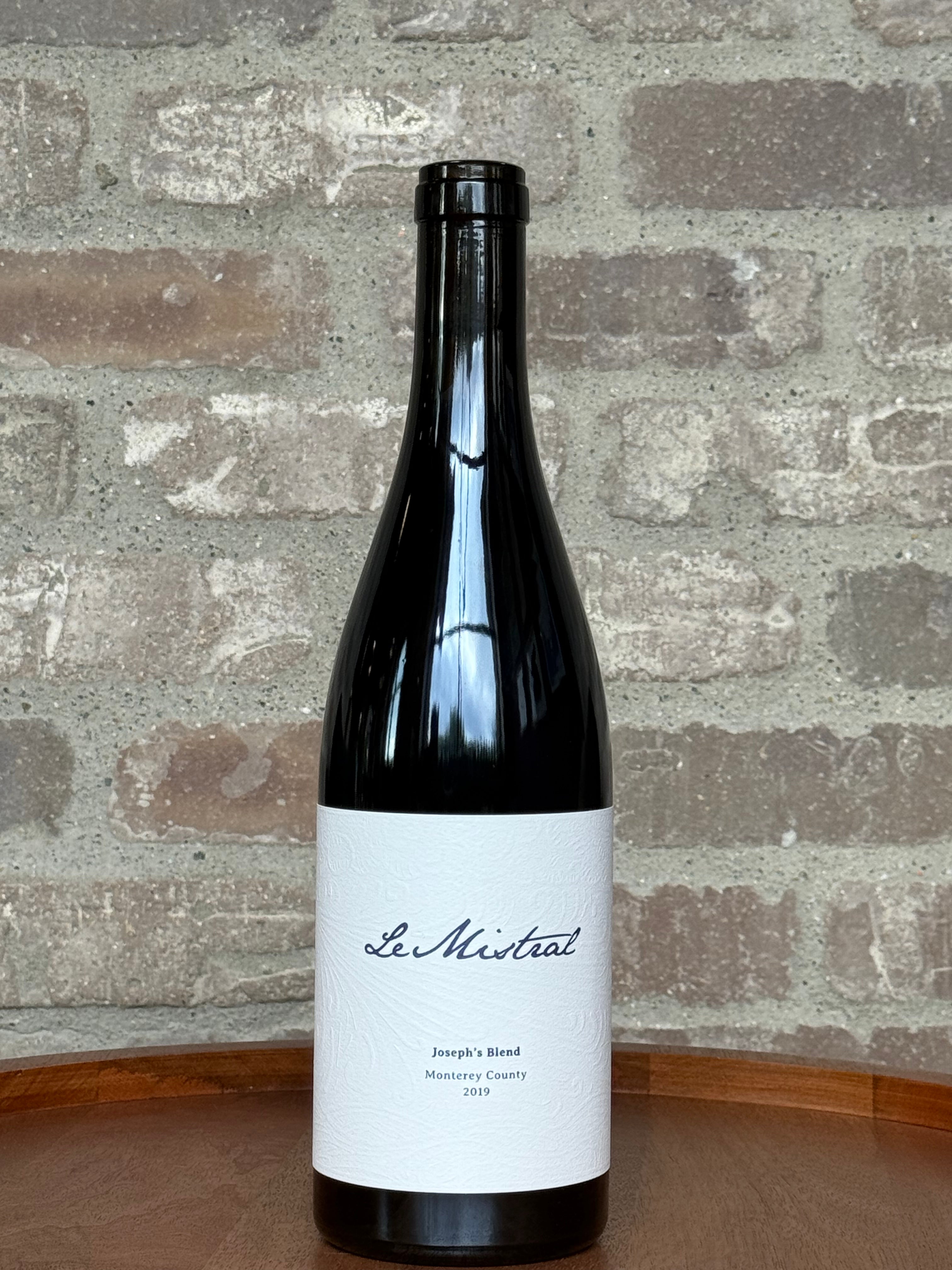 Wine bottle labeled 'Le Mistral' on a wooden surface with a brick wall background