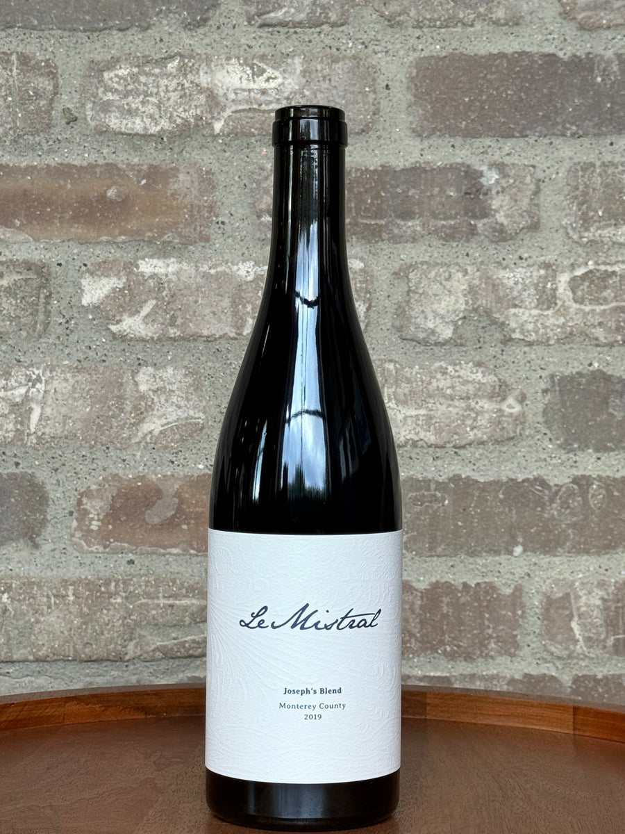 Wine bottle labeled 'Le Mistral' on a wooden surface with a brick wall background