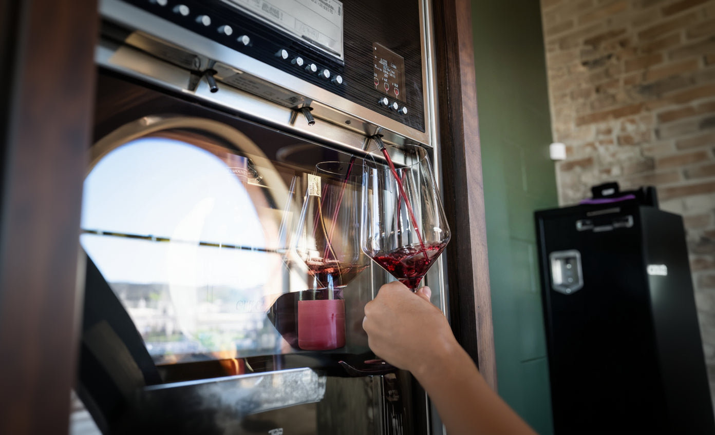 Person pouring red wine into two glasses in a kitchen.