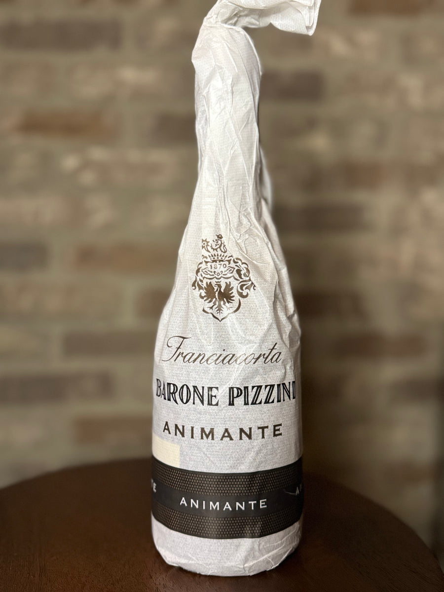 Bottle of Franciacorta Barone Pizzino Animante wrapped in paper against a brick wall.