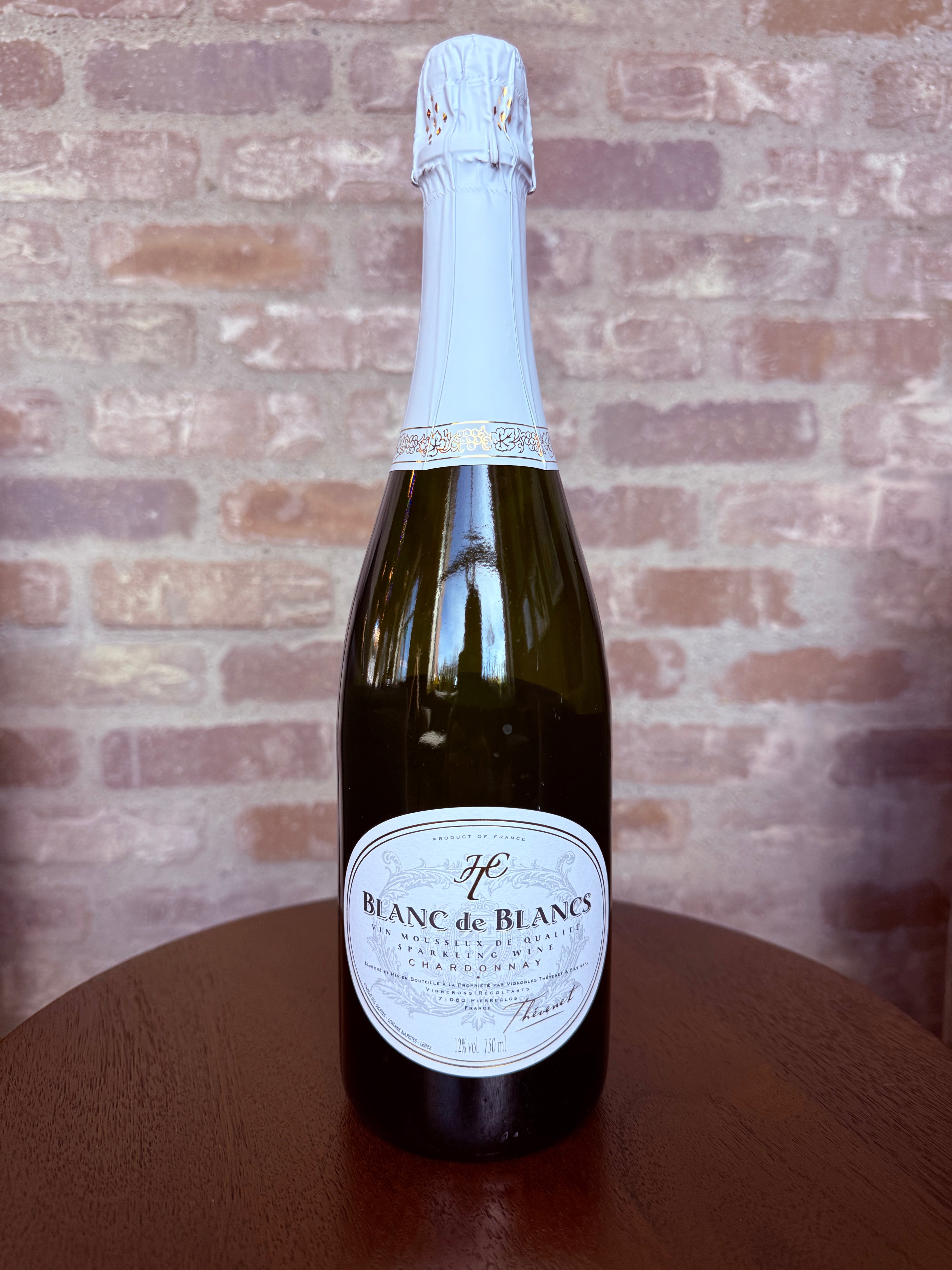 Bottle of Blanc de Blancs champagne on a wooden surface with a brick wall background